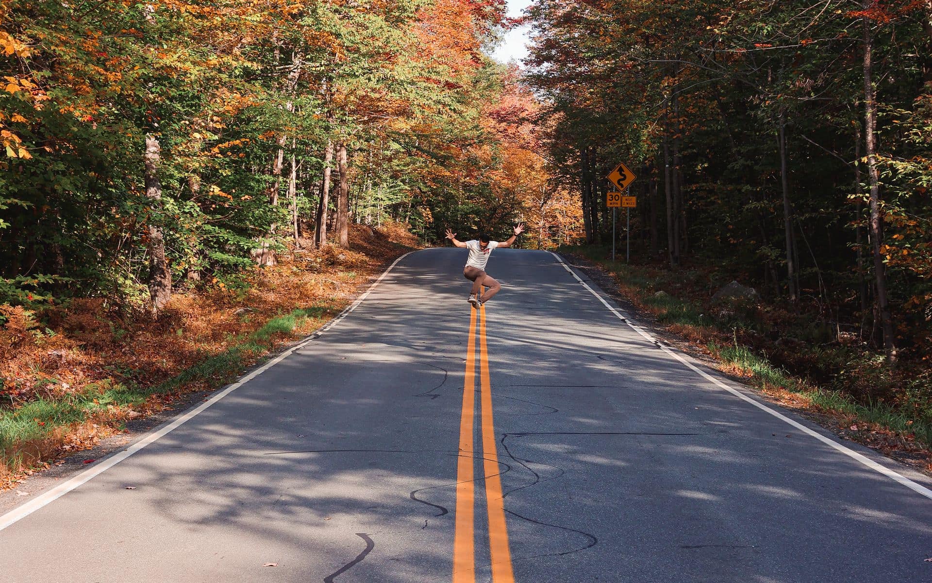 Sugar maples turning red and orange along a two-lane road in Vermont's Mad River Valley during peak fall foliage