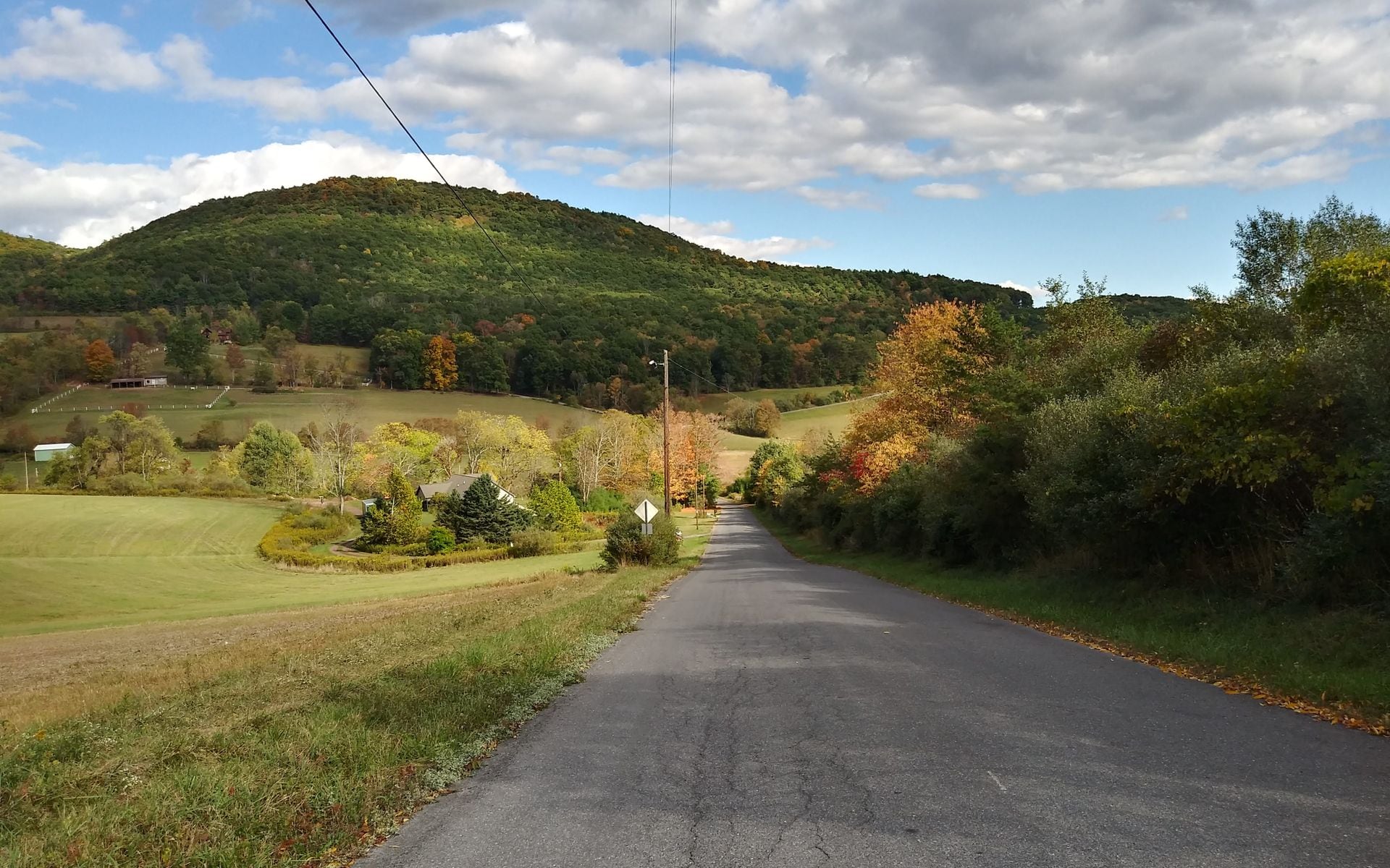 A two-lane road winding through Vermont hill farms and sugar maples in autumn color, Green Mountains visible in the background