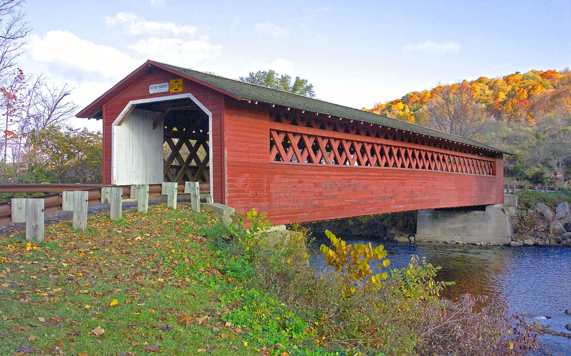 A covered bridge and autumn foliage along a Vermont back road with green hills in the background