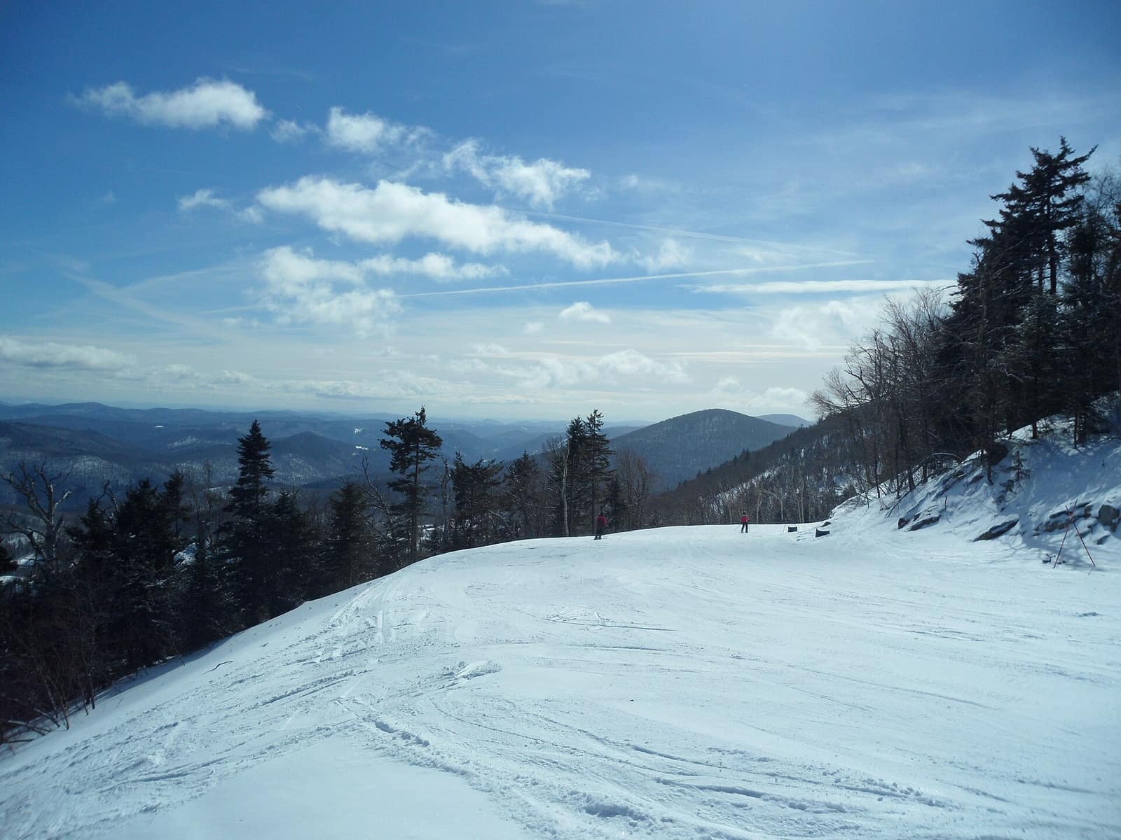 A wide snow-covered ski trail at Killington Ski Area with two skiers and Green Mountains ridgeline in the background
