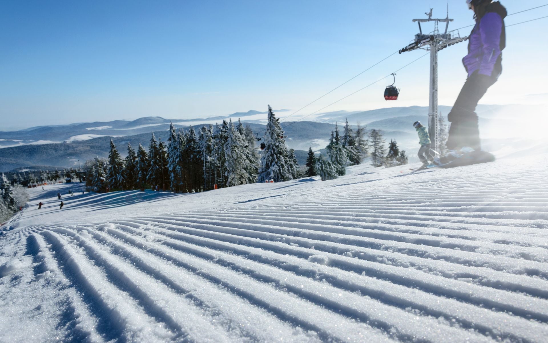 Skiers on a wide groomed trail at a Vermont mountain resort in winter, with snow-covered Green Mountains stretching into the distance