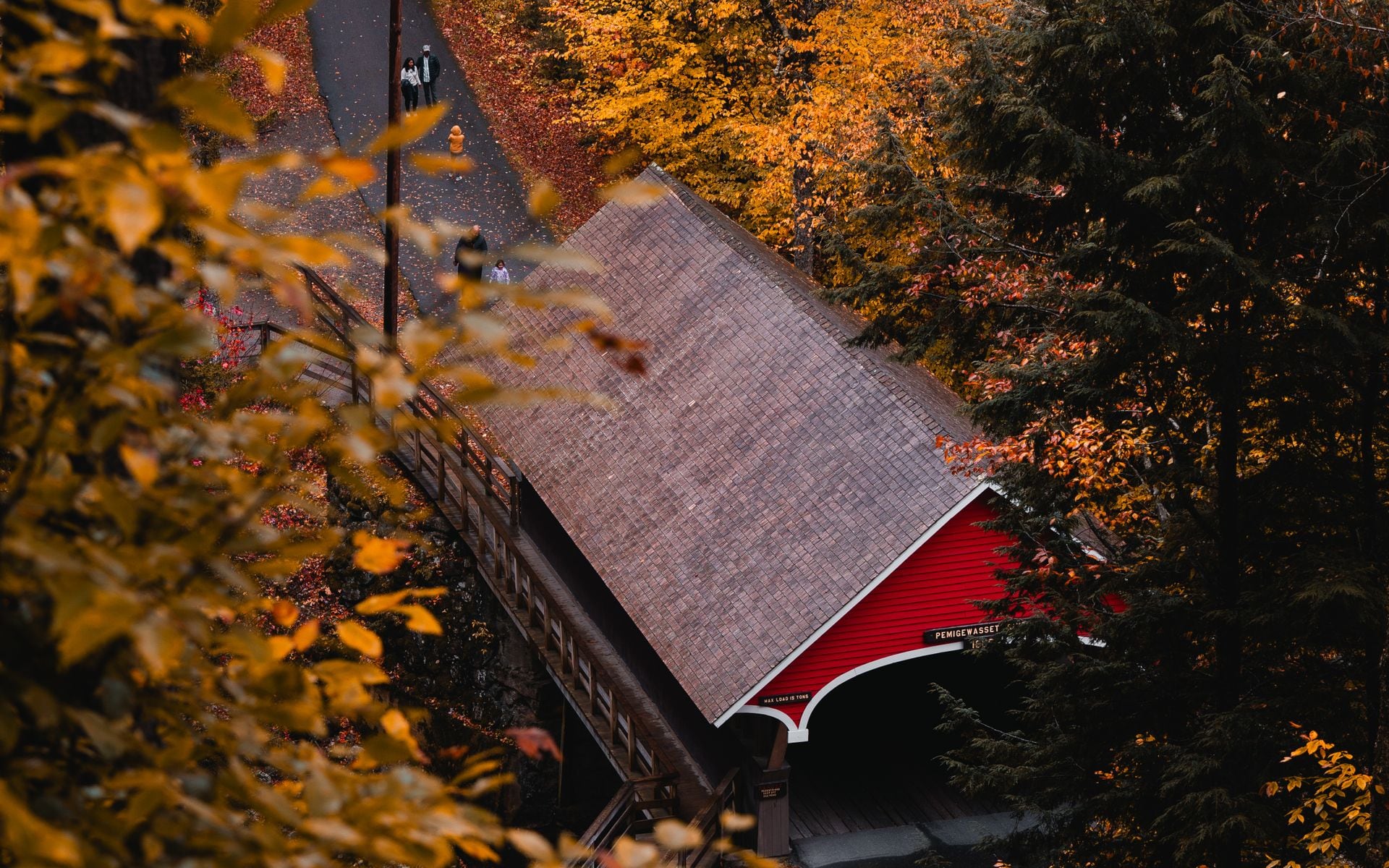 Two children walking across a covered wooden bridge in Vermont in autumn with orange and red maples overhead